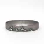 Pulsera artesanal de plata oxidada con relieve de paisaje marino y amatistas engastadas.