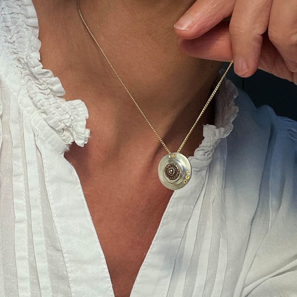 Dona amb brusa blanca mostrant un penjoll de plata rodó amb detall antic engastat i tres safirs grocs engastats, amb cadena d’or, donant un look actual i modern.