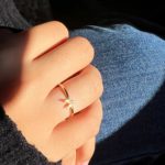 Main féminine portant une fine bague en or avec bande lisse et détail central en forme d’œil, design artisanal inspiré de l’ancien