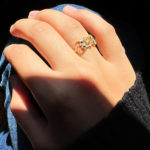 Bague fine en or avec design vintage et saphirs bleus, portée à la main d’une femme au soleil