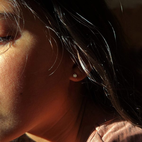 Femme portant de petites boucles d’oreilles en or, design artisanal fin inspiré vintage