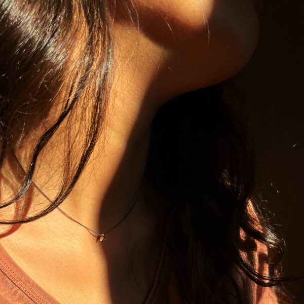 Femme portant un collier en argent oxydé avec pendentif fin en or, feuilles délicates de style ancien