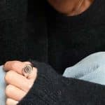 Femme portant un pull foncé montrant sa main avec une bague artisanale type chevalière, avec un détail ancien serti, apportant un look actuel et moderne.