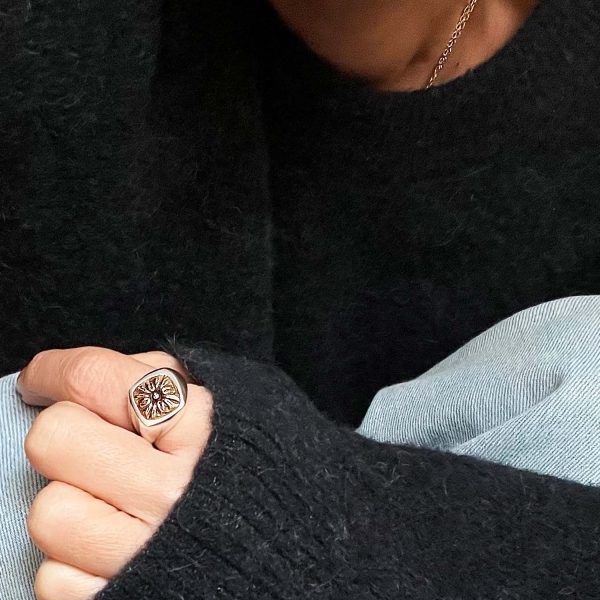 Mujer con jersey oscuro mostrando su mano con un anillo artesanal tipo sello, con un detalle antiguo engastado, dando un look actual y moderno.