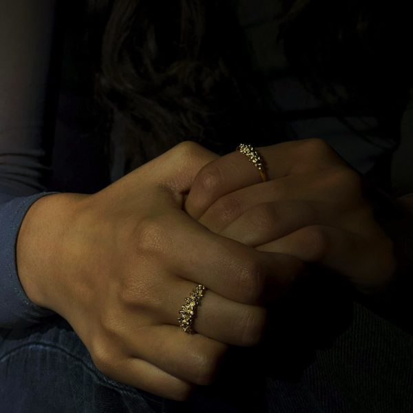 Main féminine portant une fine bague en or faite main, design de perles groupées qui capte et reflète fortement la lumière