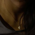 Mujer con collar artesanal de oro con colgante en forma triangular irregular de bolitas agrupadas, diseño orgánico que brilla intensamente con el movimiento