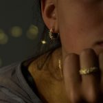 Mujer con pendientes de aro de oro artesanal con bolitas agrupadas, diseño natural y orgánico que brilla intensamente