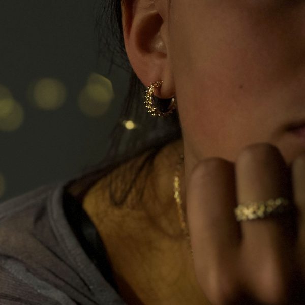 Mujer con pendientes de aro de oro artesanal con bolitas agrupadas, diseño natural y orgánico que brilla intensamente