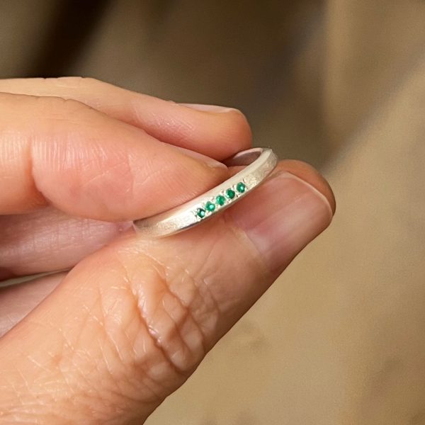 Bague fine en or blanc recyclé faite à la main, cinq émeraudes alignées serties en grain, finition mate organique.