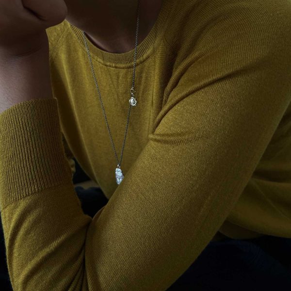 Cadena larga de plata oxidada con colgantes tipo amuleto y cierre en oro, sobre jersey mostaza