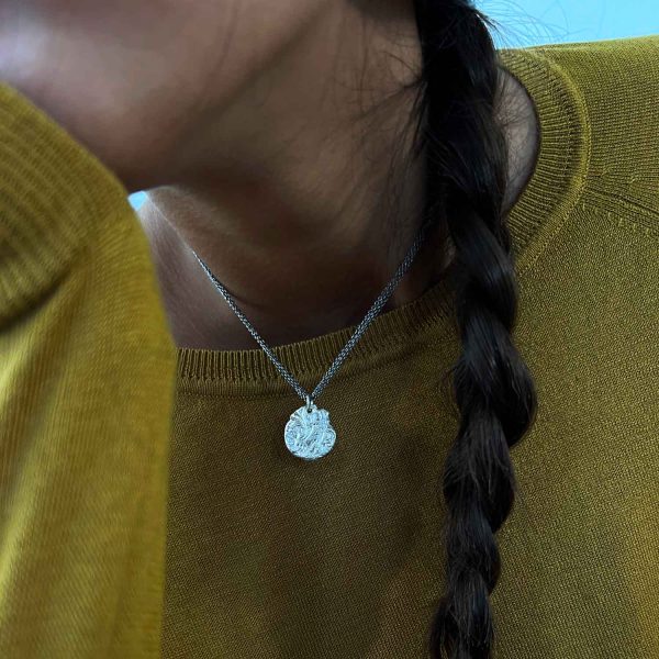 Collier en argent fait main avec pendentif rond gravé de motifs floraux anciens, porté sur un pull moutarde