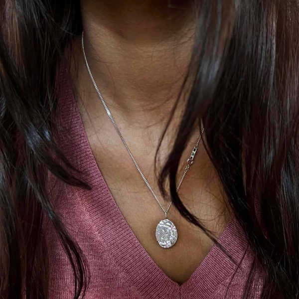 Colgante ovalado de plata con grabado vegetal antiguo y dos zafiros rosas, sobre fondo blanco neutro