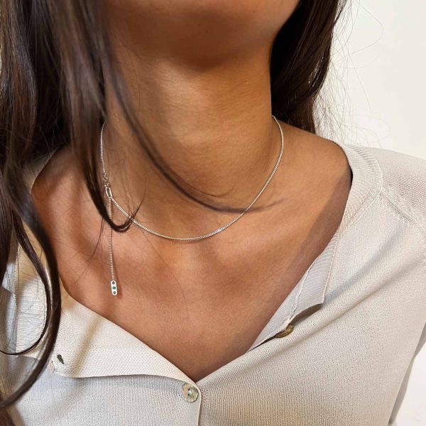 Collier en argent à plusieurs longueurs avec fermoir apparent orné d’une émeraude, porté sur une chemise beige