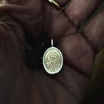 Main dans l’atelier tenant un pendentif artisanal avec détail ancien serti.