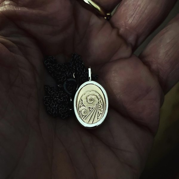 Main dans l’atelier tenant un pendentif artisanal avec détail ancien serti.