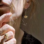 Femme portant des boucles d’oreilles en argent plaqué or avec fleur étoilée et une bague assortie.