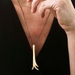 Femme portant un pendentif allongé en argent plaqué or au design stylisé et fluide.