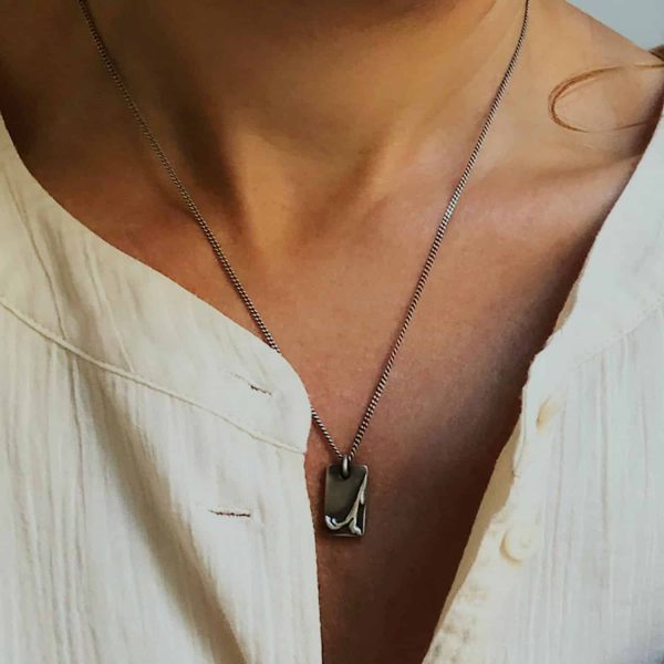 Dona amb collaret artesanal de plata oxidada amb medalla rectangular amb relleu inspirat en paisatge natural.