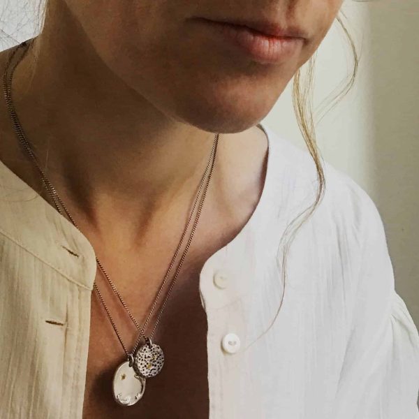 Mujer con collares artesanales de plata uno con medalla ovalada con relieve de ola de mar y citrino engastado y otro con medalla inspirada en piedra erosionada con citrinos engastados ambos llevados en superposición.