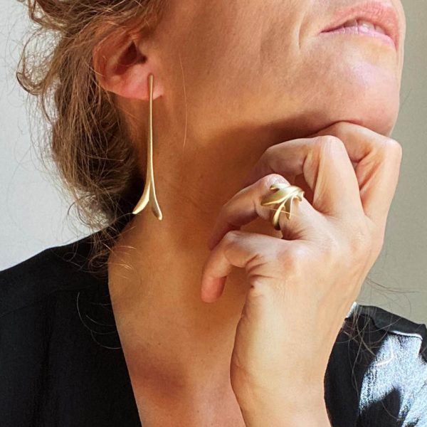 Mujer llevando pendiente largo de plata chapada en oro con diseño estilizado y elegante.